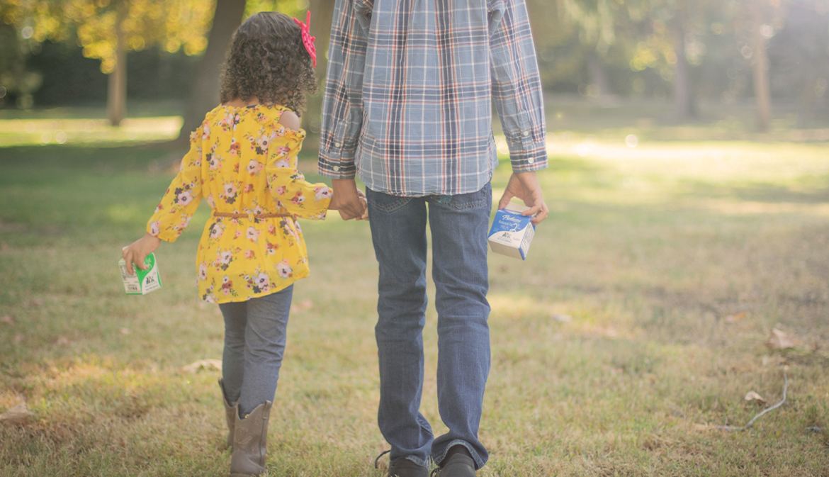 Brother and sister holding hands while drinking milk in a park walking away