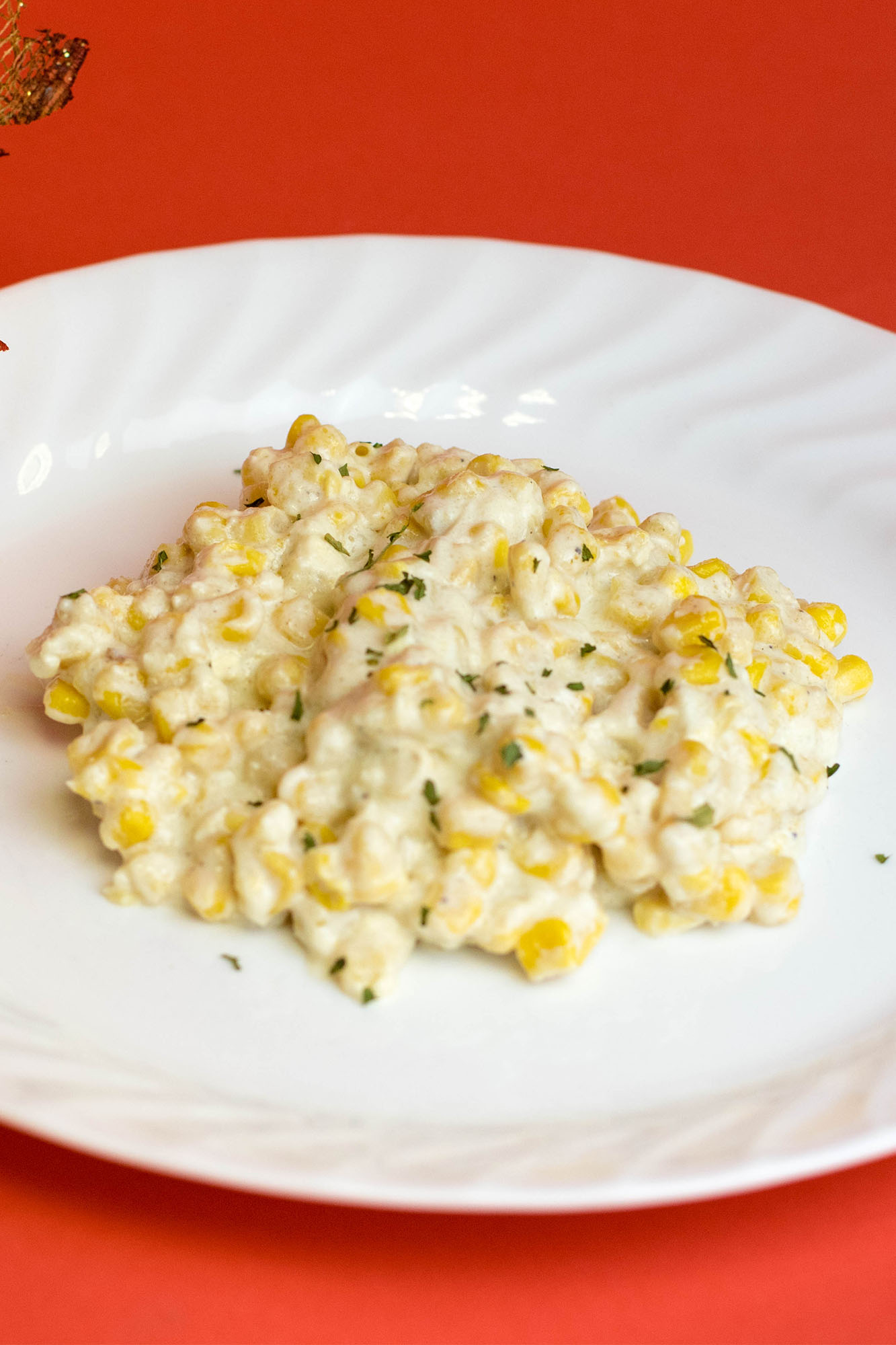 CreamedCorn_Horizontal Creamed corn on a white plate laying on a flat red background.