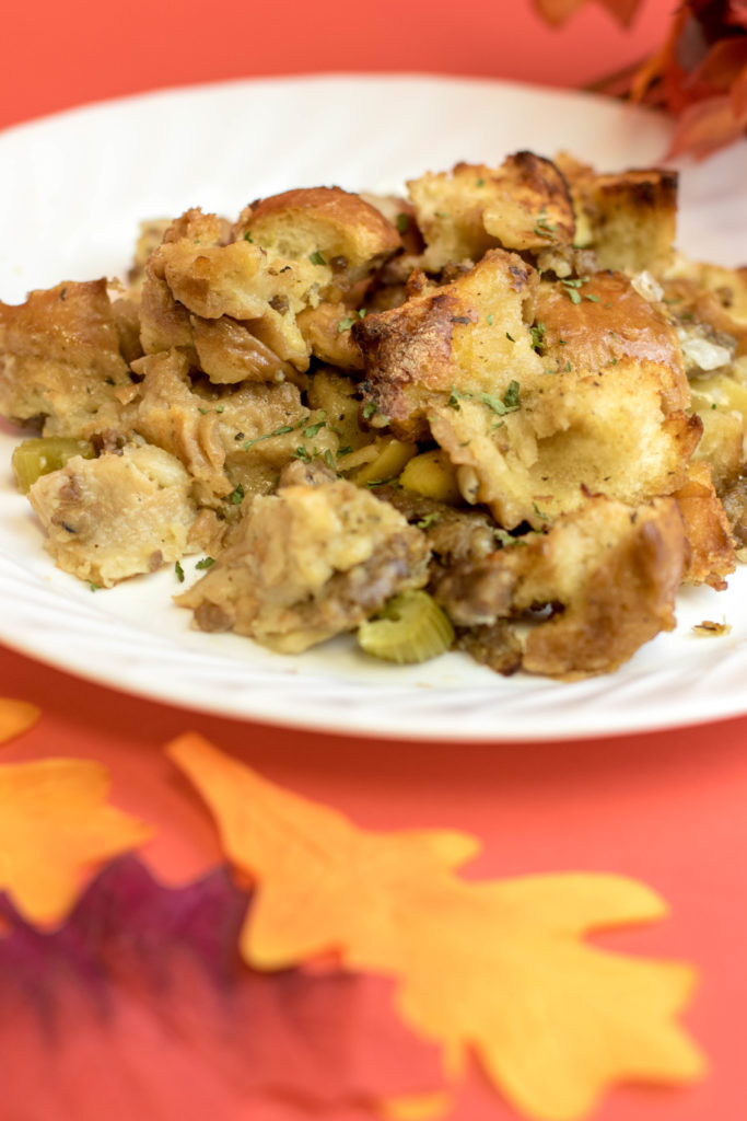 NOVDEC_Recipes (2 of 10) Thanksgiving stuffing on a white plate surrounded by fall leaves sitting on a red background.