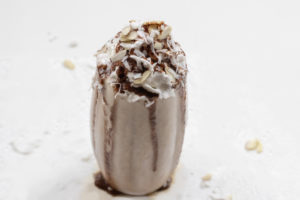 Chocolate Milkshake with whipped topping, sliced almonds, and shredded coconut on a white background.