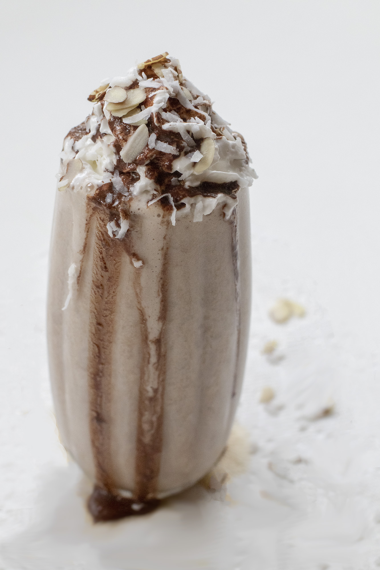 1Y8A7217 Chocolate Milkshake with whipped topping, sliced almonds, and shredded coconut on a white background.