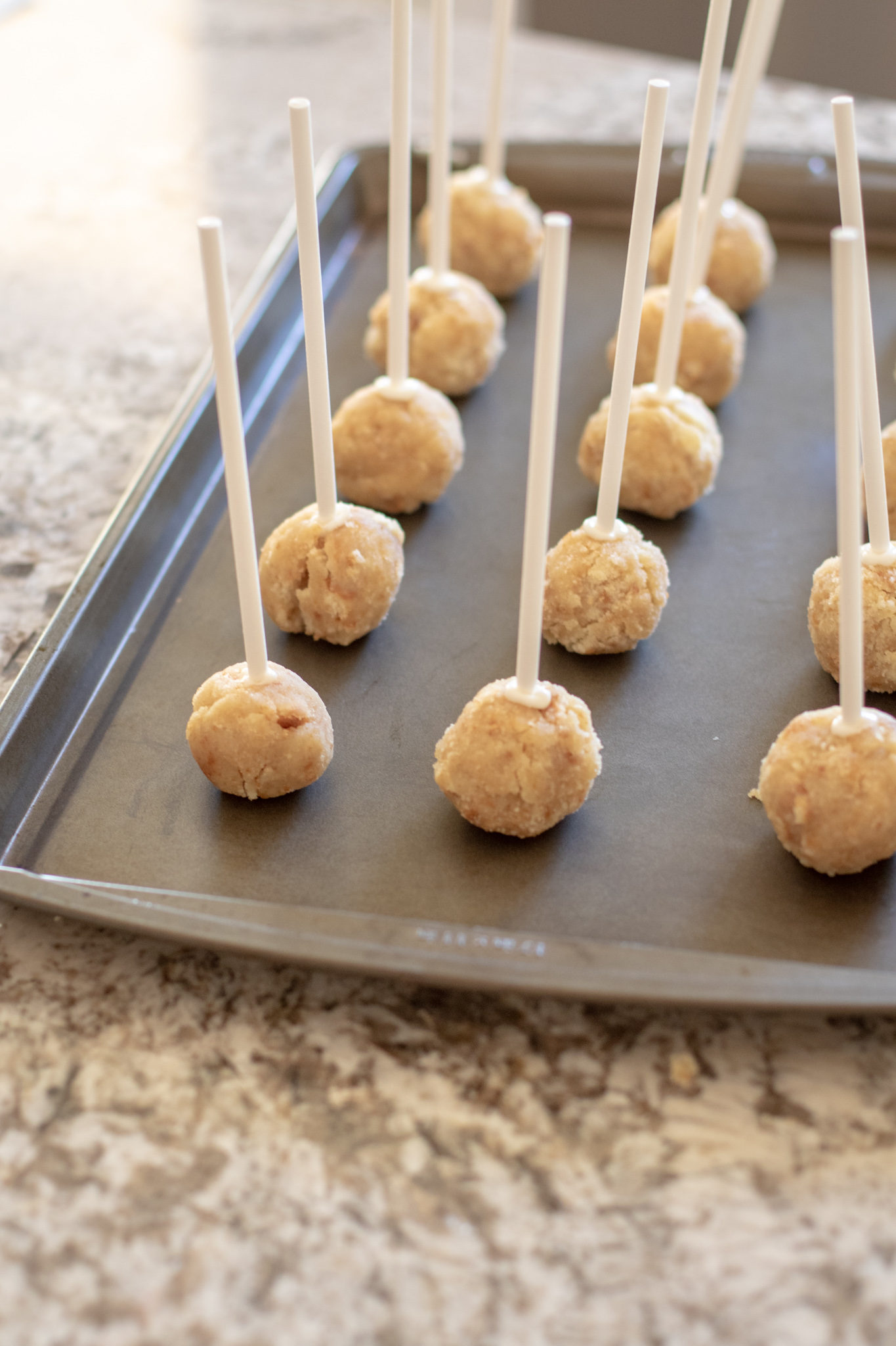 Cake rolled into balls on popsicle sticks sitting on a cookie sheet.
