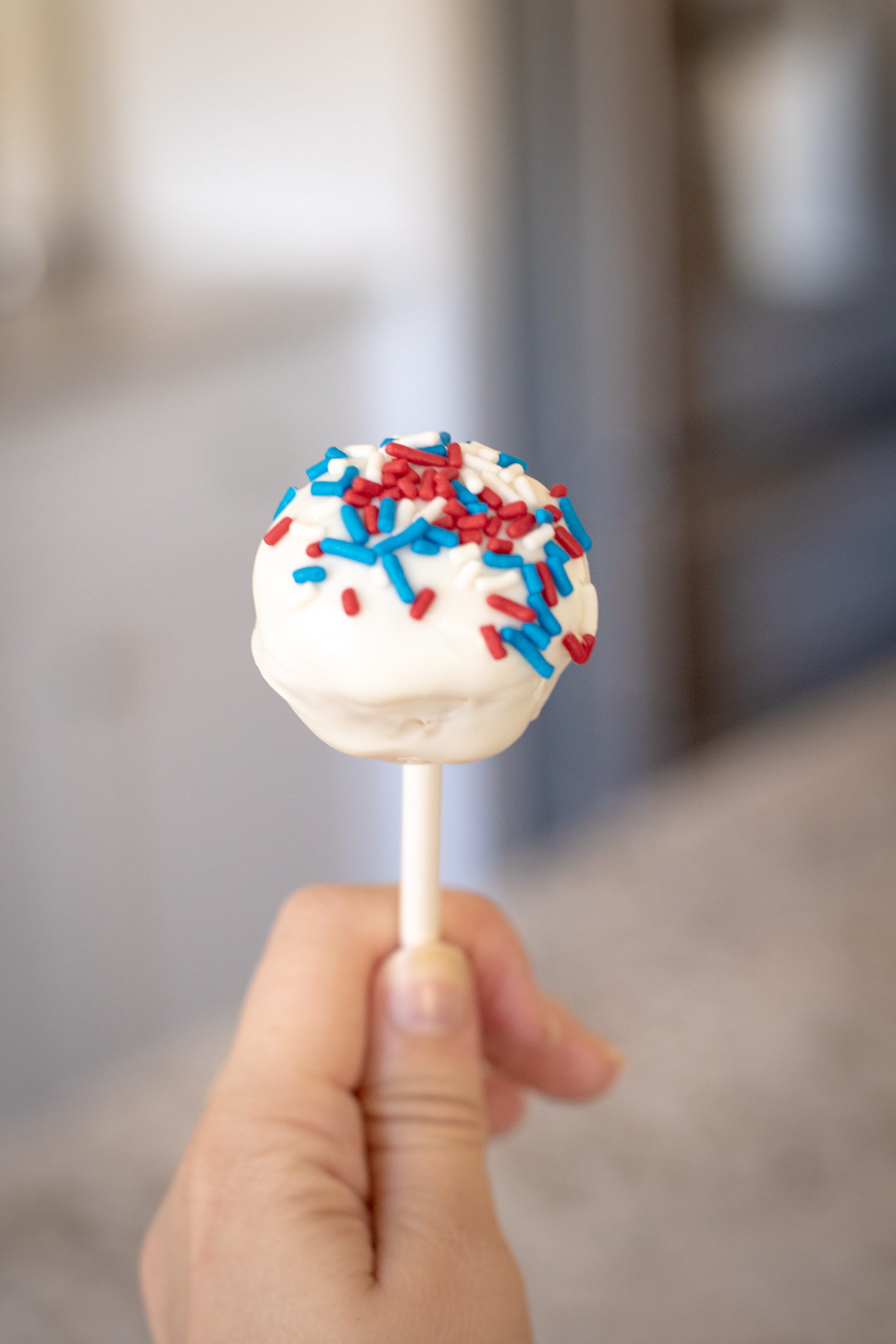 Someone holding a cake pop with red white and blue sprinkles on it.